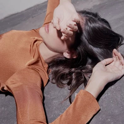 Woman in a terracotta top lying down with one hand covering her eyes