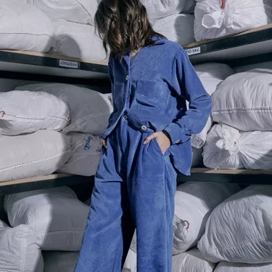 Woman in a blue corduroy set standing in front of shelves of white bundles