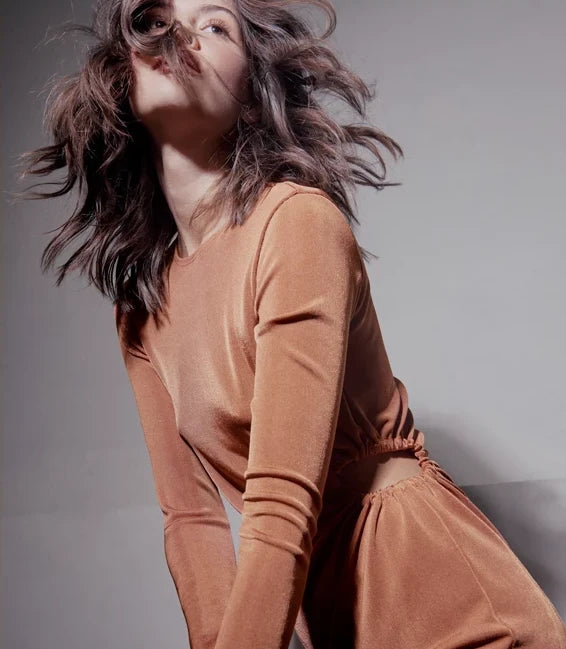 Model with windswept hair wearing a terracotta long-sleeve top